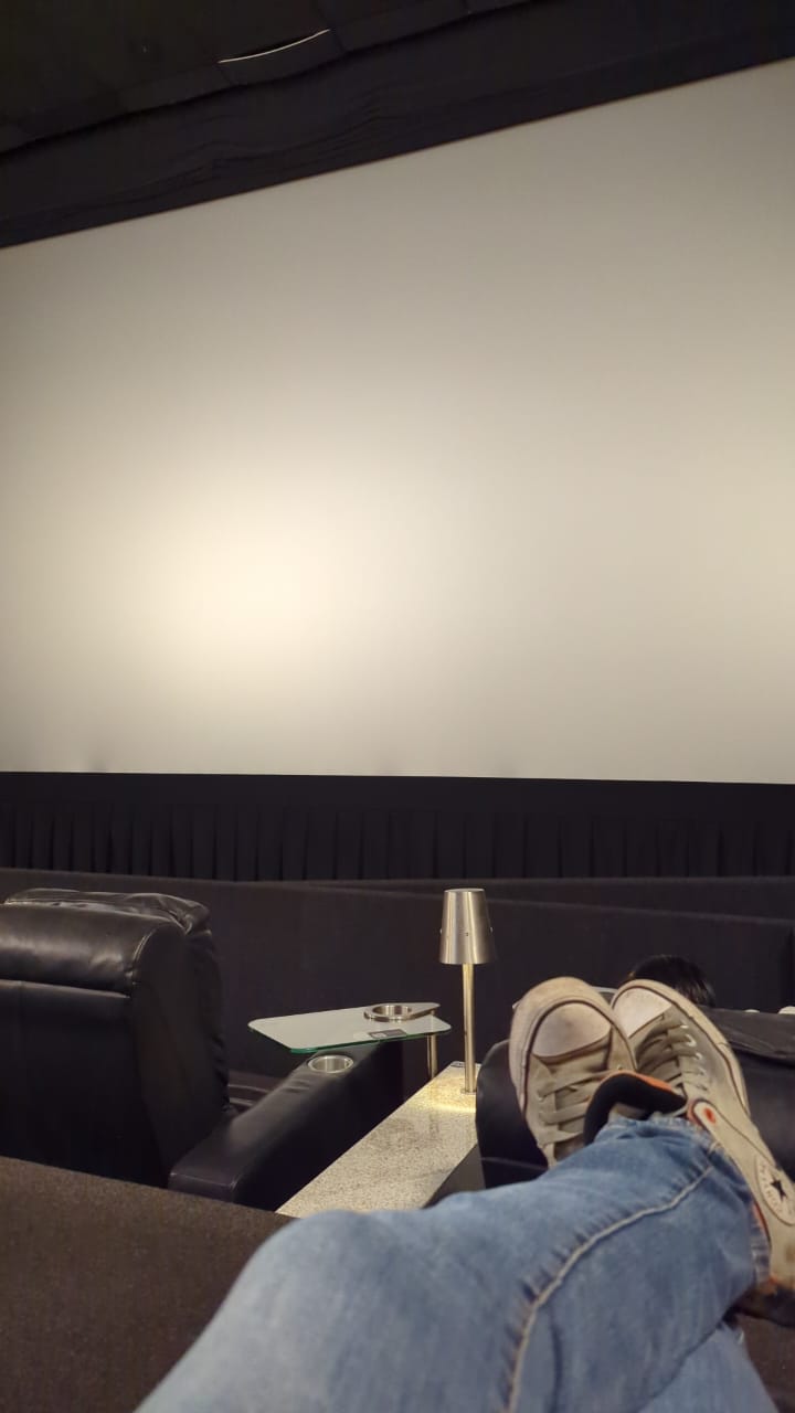 Feet up on a leather recliner in a Cinemex VIP theater, facing the blank screen before the ads begin